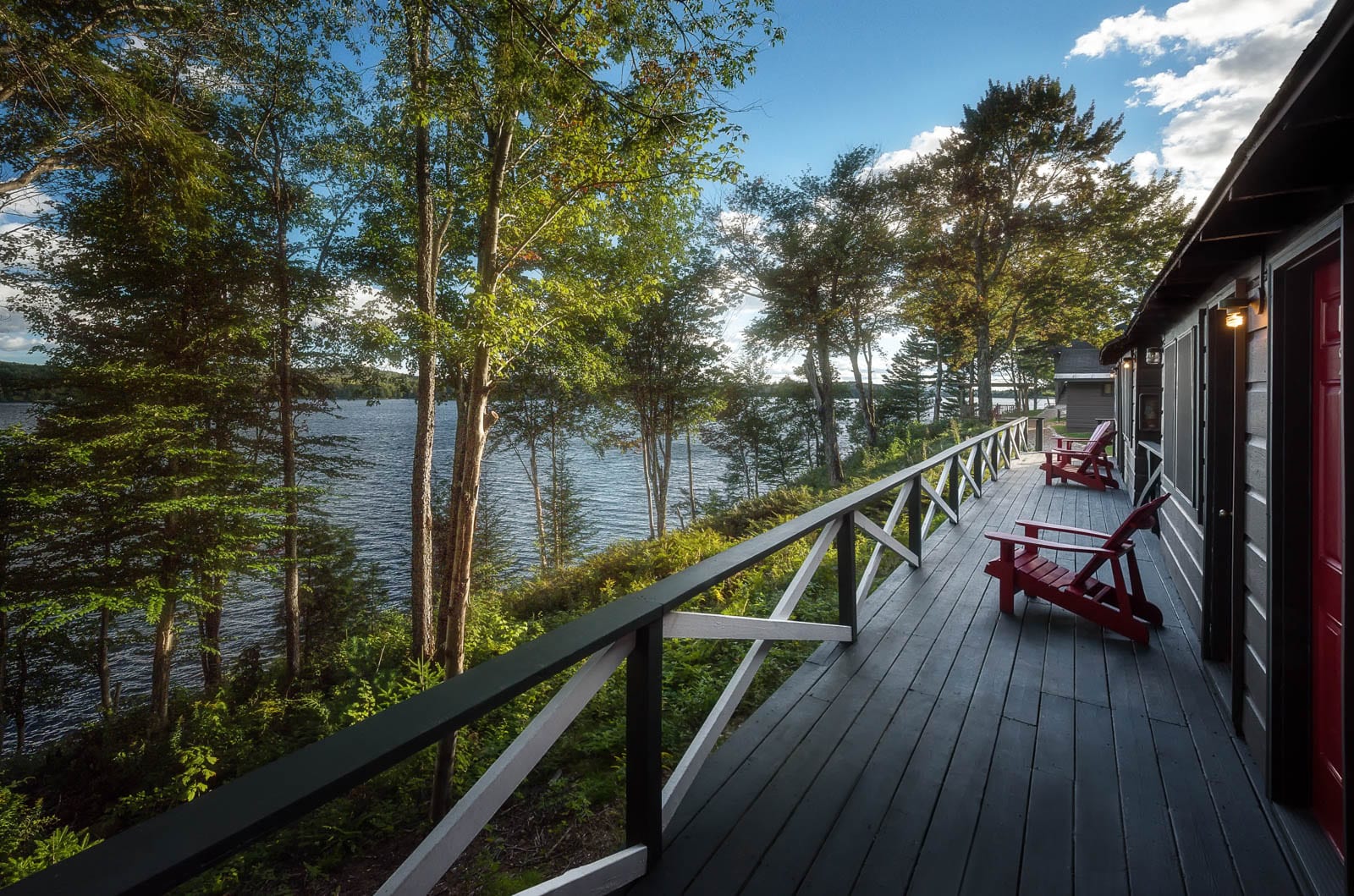 A deck with red chairs overlooking a lake.