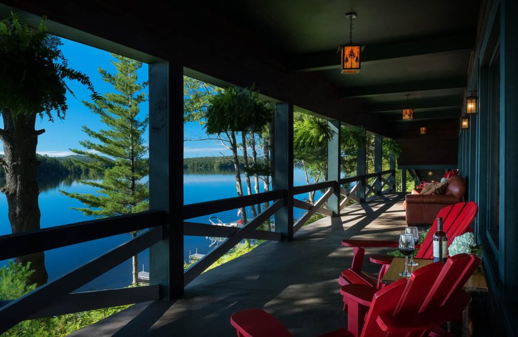 A porch with red chairs and a view of a lake.