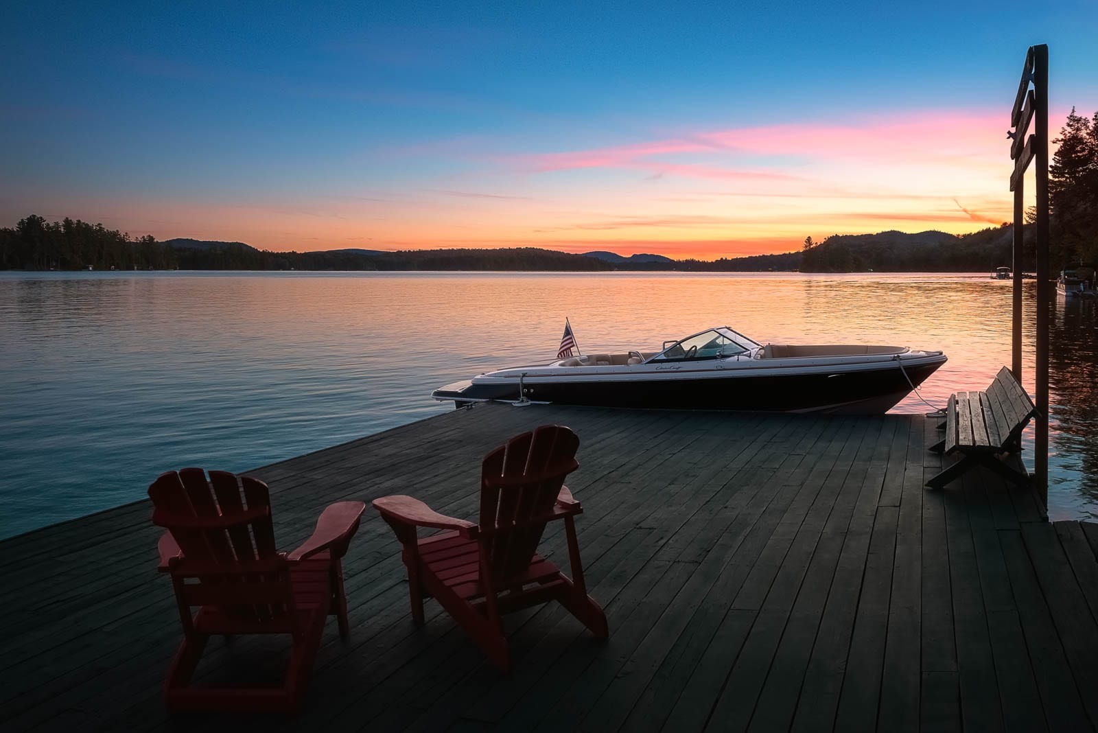 A dock with a boat and red chairs at sunset.