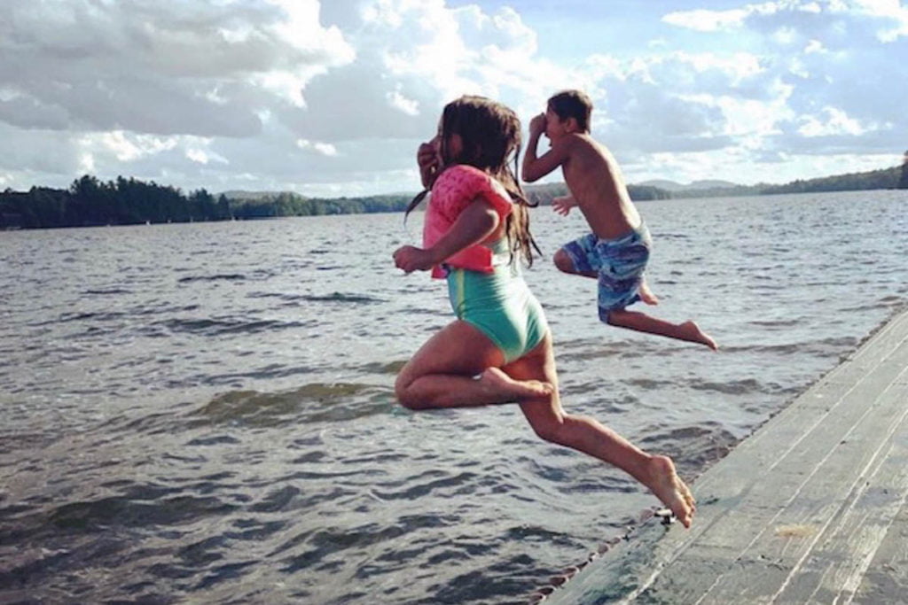 Two children jumping off a dock into a body of water.