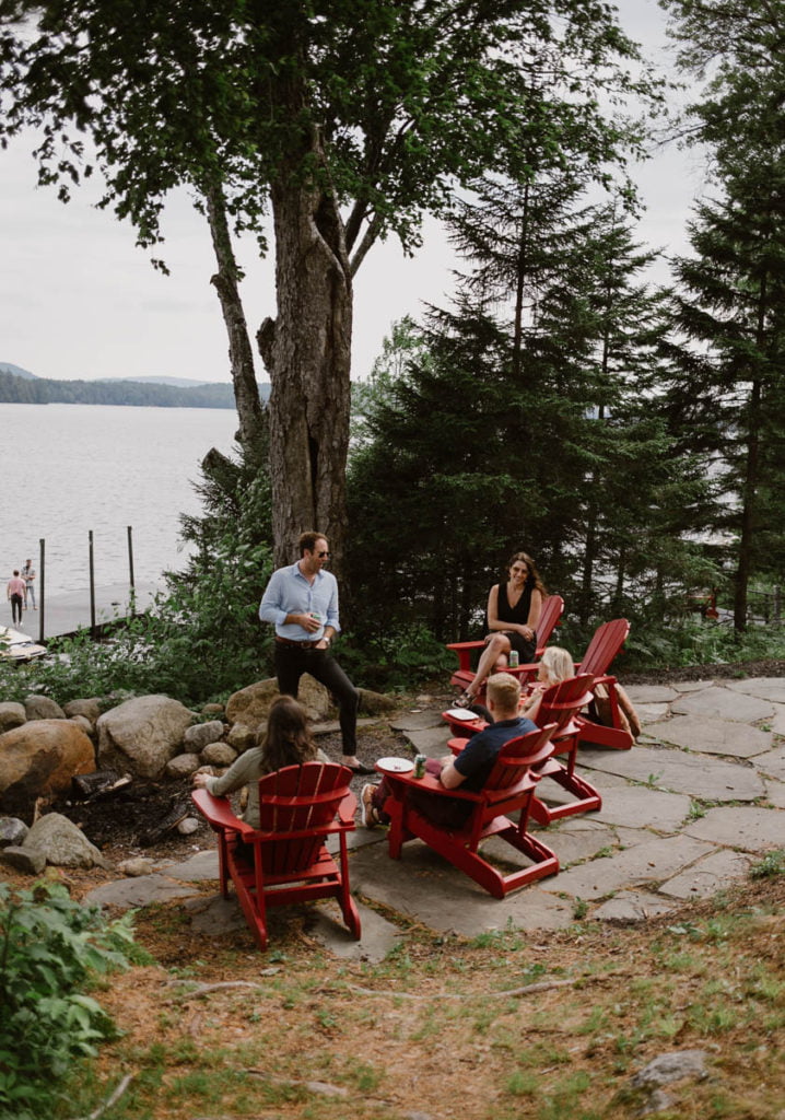 A group of people sitting around a fire pit near a lake.
