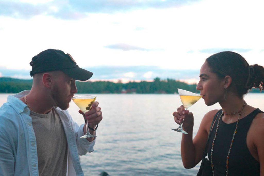 A man and woman drinking martinis near a body of water.